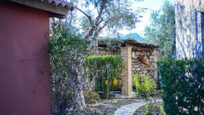 Un edificio de piedra con tejado de paja, rodeado de abundante vegetación y un sendero de piedra.
