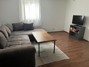 A modern living room with a sectional sofa, a wooden coffee table, and a television on a stand.