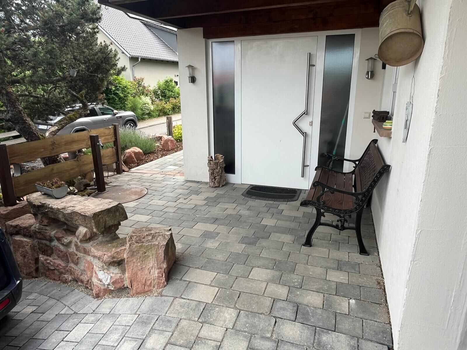 A patio with a stone floor, a wooden bench, a metal chair, and a car parked outside.