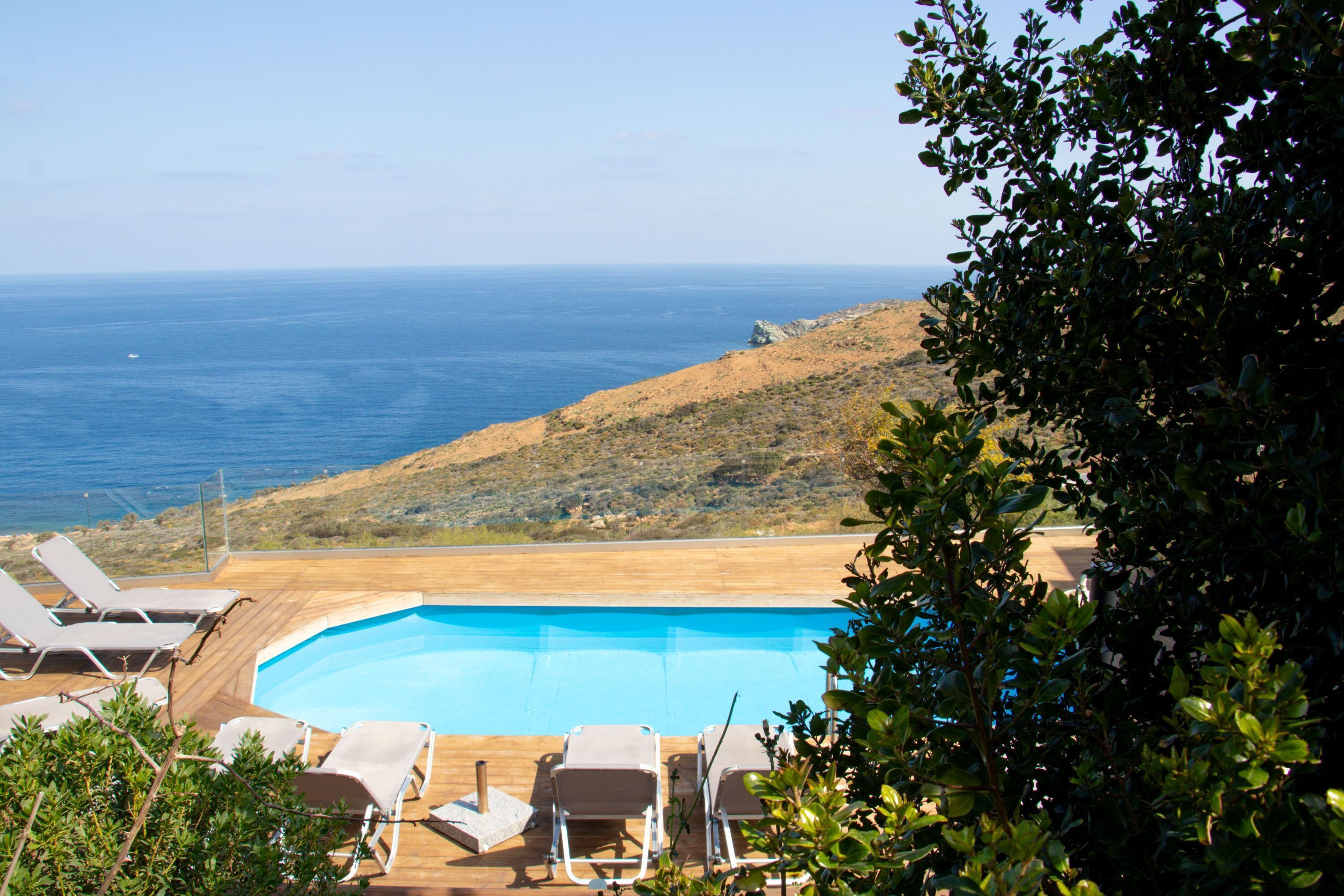 Piscina com espreguiçadeiras, vista para o oceano e um morro.