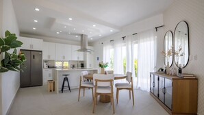 A modern kitchen with white cabinets, a stainless steel refrigerator, and a dining area with a wooden table and chairs. - Sosua Ocean Village Villa 24 (Cabarete)