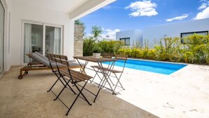 A modern outdoor pool area with a table and chairs, a sliding glass door, and a view of the surrounding buildings and greenery. - Sosua Ocean Village Villa 24 (Cabarete)