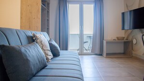 A living room with a sofa, a flat-screen TV, a wooden column, a sliding glass door, and a small table with a bowl. - House of Harmony Suites | Luca (Agia Pelagia)