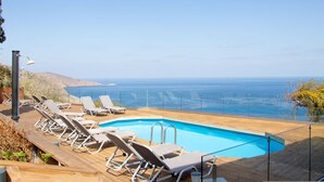 A poolside area with lounge chairs and a view of the ocean. - House of Harmony Suites | Luca (Agia Pelagia)