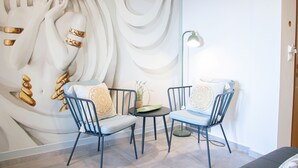 A room with a mural, two chairs, a small table, and a floor lamp. - House of Harmony Suites | Luca (Agia Pelagia)