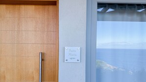 A wooden door with a metal handle, a sign reading "Suite Maria", and a view of the sea through a window. - House of Harmony Suites | Maria (Agia Pelagia)