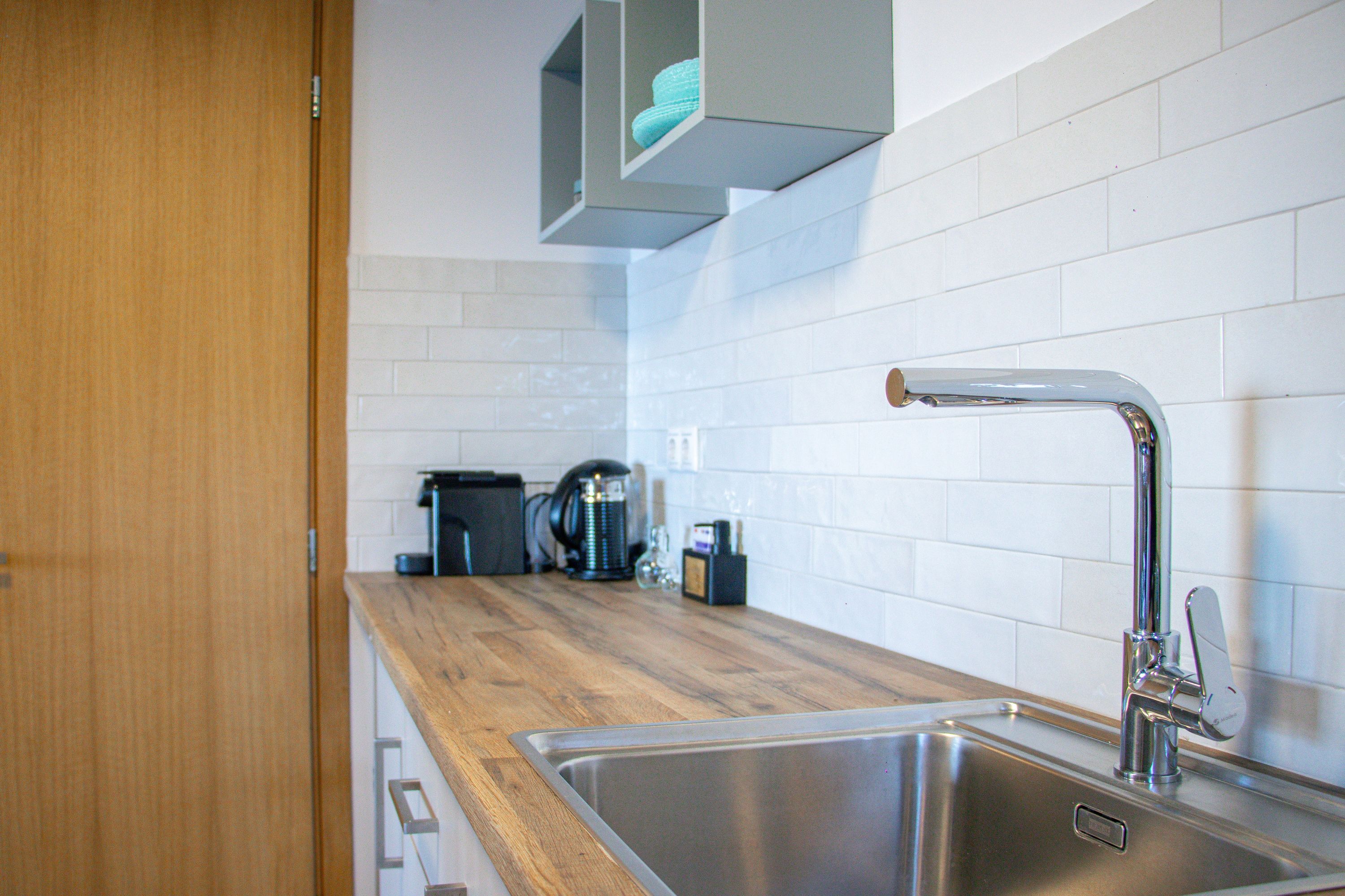 A modern kitchen with a stainless steel sink, wooden countertop, and white tiled backsplash.