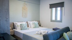 Een slaapkamer met een bed, nachtkastje, dressoir, raam met zonwering en wanddecoratie van macramé.