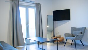 Een moderne woonkamer met een bank, salontafel, stoel, een aan de muur bevestigde flatscreen-tv en een grote spiegel.