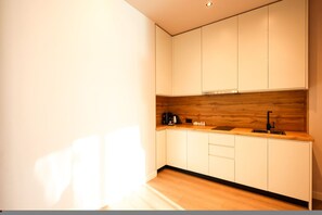 A modern kitchen with white cabinets, a wooden backsplash, and a black faucet. - Zins Luxury Apartment 07 (Durrës)