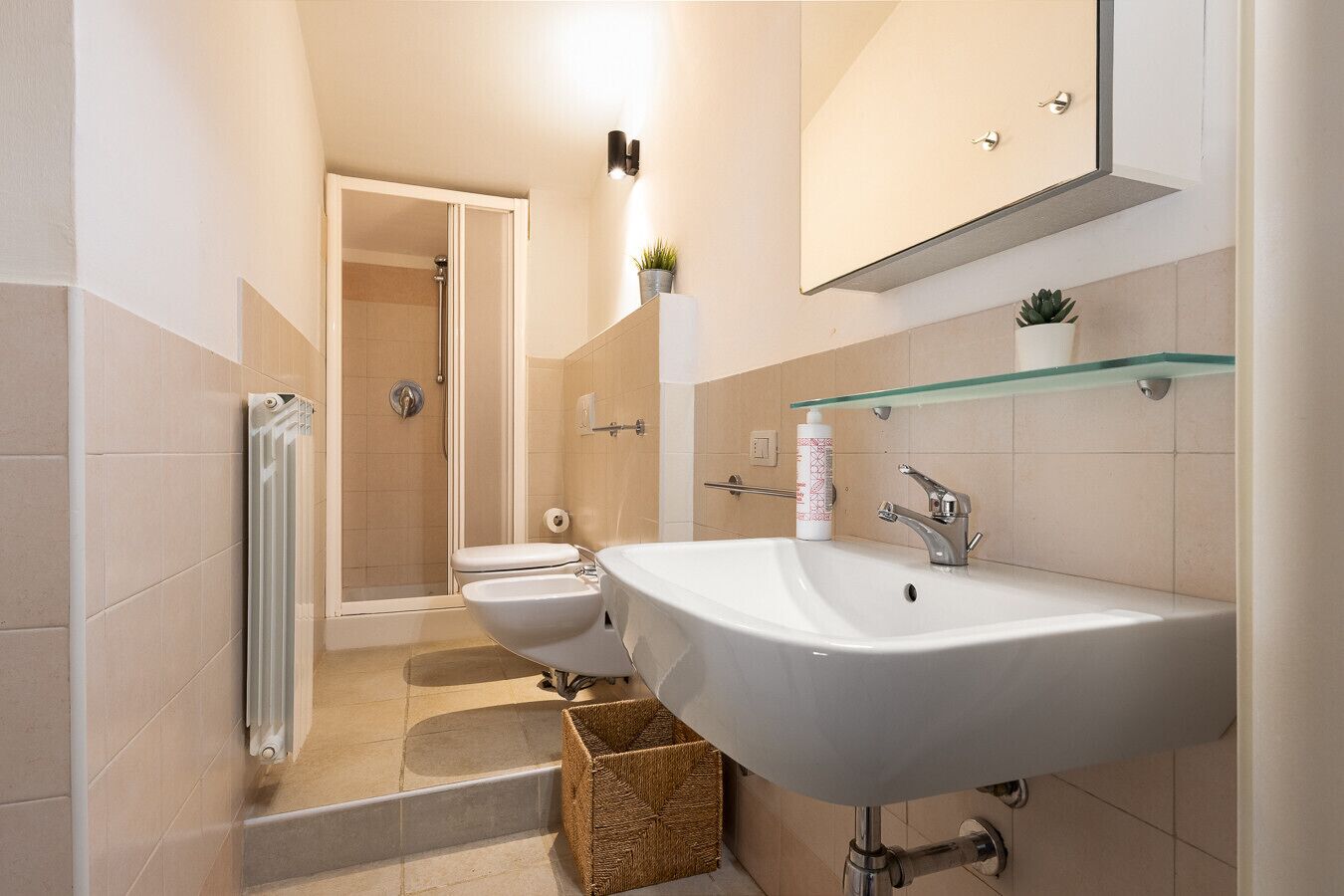 Une salle de bain moderne avec un lavabo blanc, une étagère en verre au-dessus du miroir et un espace douche.