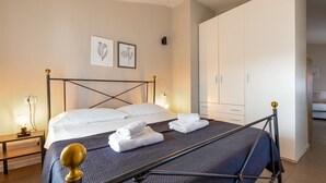 A neatly made bed with white linens and rolled towels, a bedside table with a lamp, and a wardrobe with a mirror. - Desenzano Suites - Tiglio by Wonderful Italy (Desenzano del Garda)