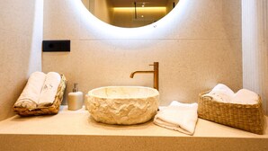 Ein Badezimmer mit einem runden, strukturierten Waschbecken, einem goldenen Wasserhahn und zwei Korbkörben mit Handtüchern.