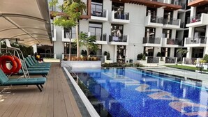 Ein Schwimmbecken mit gefliestem Boden, umgeben von einer Holzterrasse und Liegestühlen.