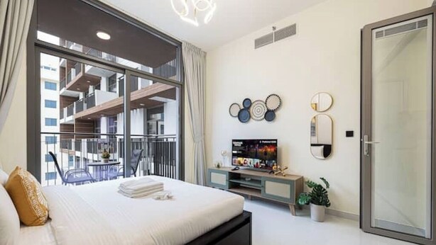 Ein modernes Hotelzimmer mit einem großen Bett, einem Fernseher, einem Balkon mit Blick auf das Gebäude und dekorativer Wandkunst.