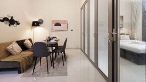 Ein modernes Wohnzimmer mit einer Couch, einem Esstisch, Stühlen und einer Glastür zum Schlafzimmer.
