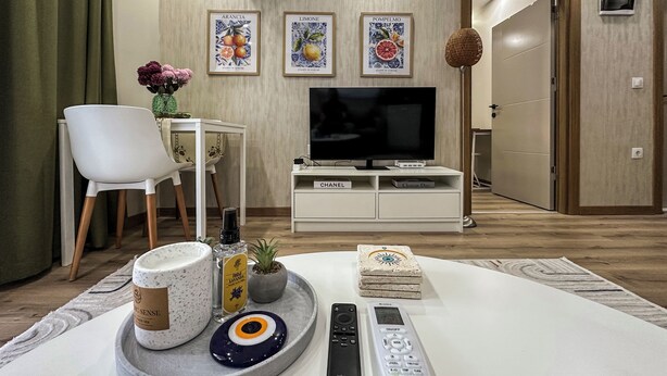 A hotel room with a TV, a remote control, a tray with a candle, a bottle of lotion, and a decorative item on the floor. - Smartly Designed Cozy Central 1BR Apartment (Antalya)
