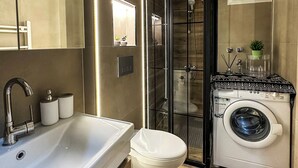 A modern bathroom with a large sink, toilet, and washing machine. - Smartly Designed Cozy Central 1BR Apartment (Antalya)