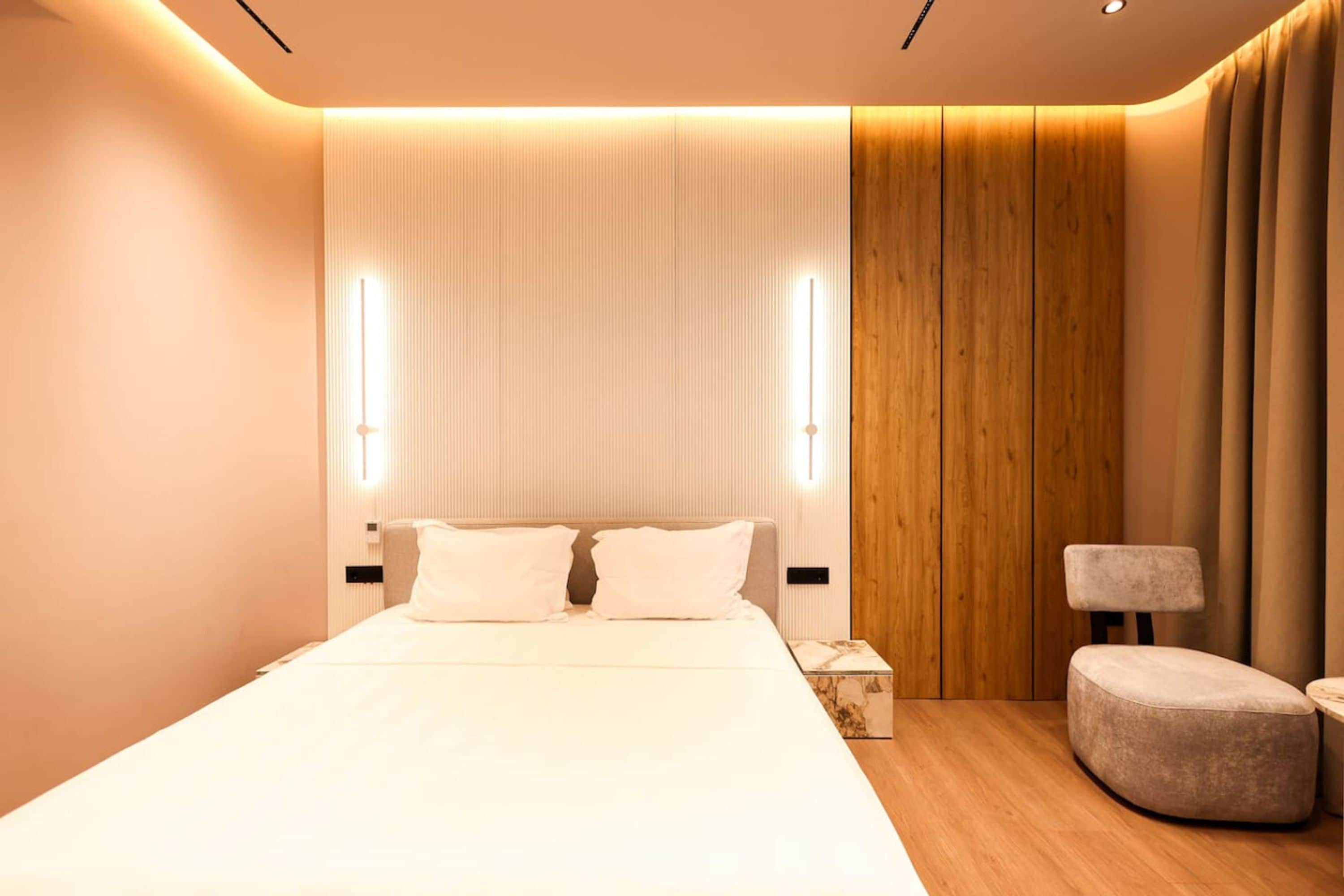 A modern hotel room with a large bed, a wooden accent wall, and a small seating area.