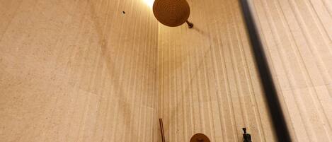 A shower area with a handheld showerhead, a wall-mounted control knob, and a bottle of shampoo.