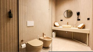 Ein modernes Badezimmer mit beiger Farbgebung, einem runden Spiegel, einem Bidet, einer Toilette und einem Waschtisch mit Spüle und Handtuchhalter.