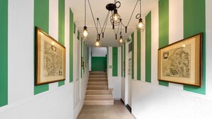 Ein Korridor mit grün-weißen Wänden, gerahmten Bildern, einer Treppe und hängenden Leuchten.
