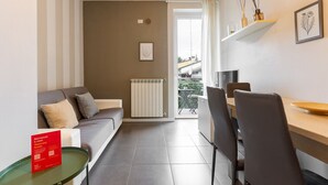 Ein modernes Wohnzimmer mit einer Couch, einem Esstisch mit Stühlen, einer Heizung und einem Balkon mit Blick.