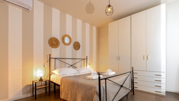 A bedroom with a bed, bedside lamps, a wardrobe, and decorative wall mirrors. - Desenzano Suites - Assenzio by Wonderful Italy (Desenzano del Garda)