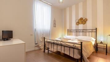 Un dormitorio con cama, mesita de noche, televisor y ventana con cortinas.