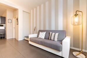 Un salon moderne avec un canapé gris et blanc, une lampe sur pied et un mur à rayures.