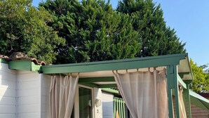 A small, private outdoor seating area with a wooden deck, a covered patio, and a view of a forested area.