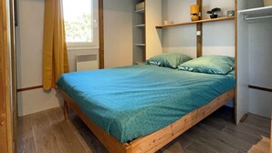 A bedroom with a wooden bed, a window with curtains, built-in shelving, and a radiator.