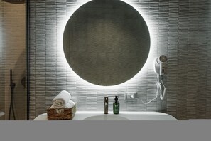 A bathroom with a round mirror, a white sink, a hairdryer, and a basket of towels. - Zins Luxury Apartment 01 (Durrës)