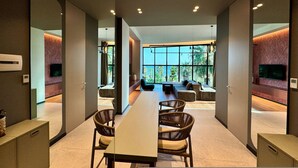 Un espace repas moderne avec une longue table, des chaises en osier et une vue sur l’extérieur grâce à de grandes fenêtres.