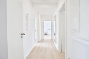 A bright, narrow hallway with white walls and light wooden flooring, leading to a room with a white door and a visible air conditioning unit. - Baltic Sea Suite 1 - Sea view & 2 balconies | Only 60 m to the beach (Timmendorfer Strand)