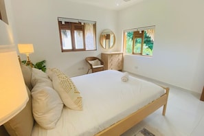 Un dormitorio con una cama, una silla, un tocador, un espejo y dos ventanas.