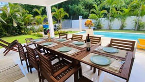 Un área de comedor al aire libre con una piscina al fondo.