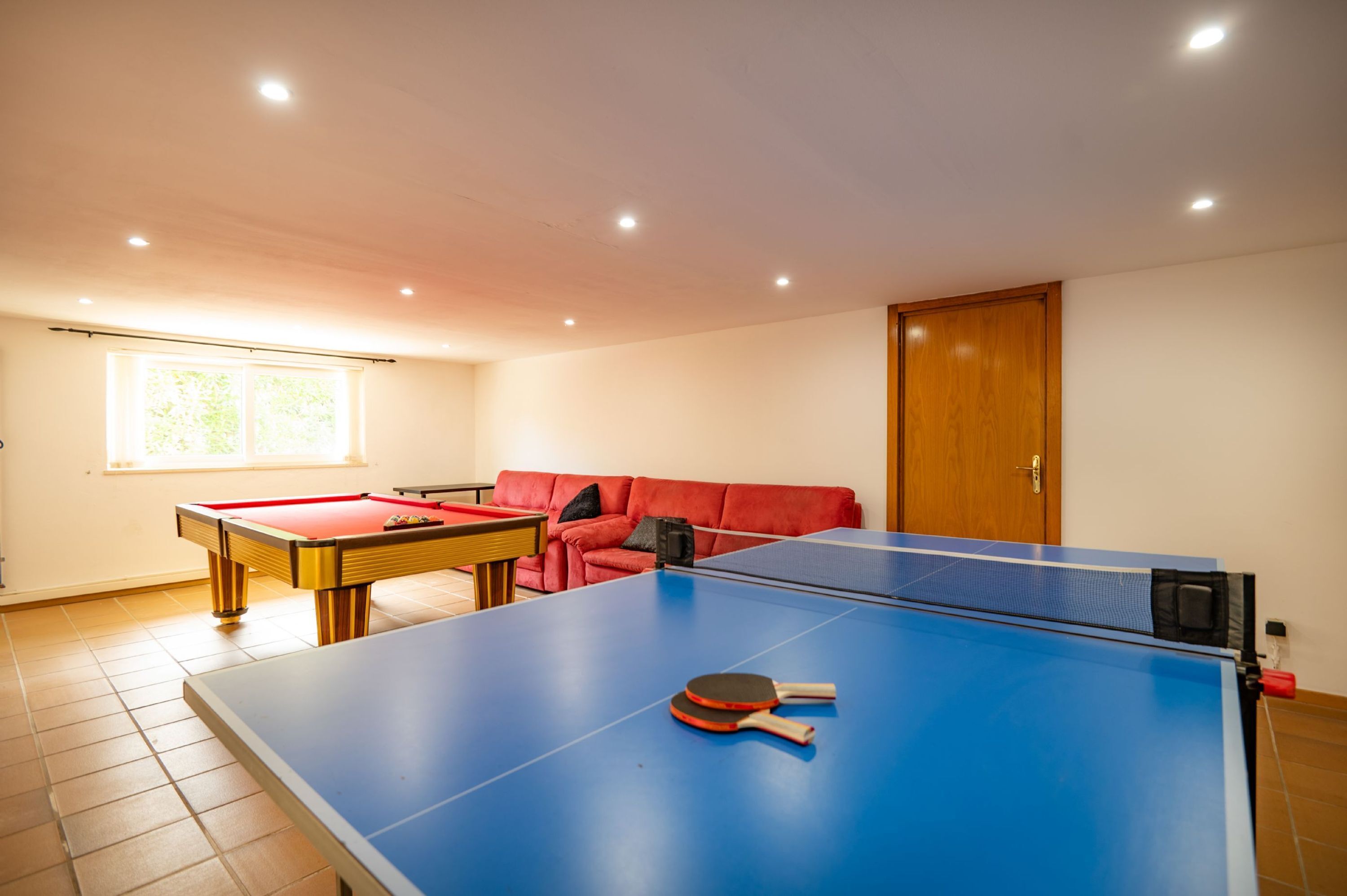Ein Zimmer mit Tischtennisplatte, Billardtisch und einem roten Sofa.