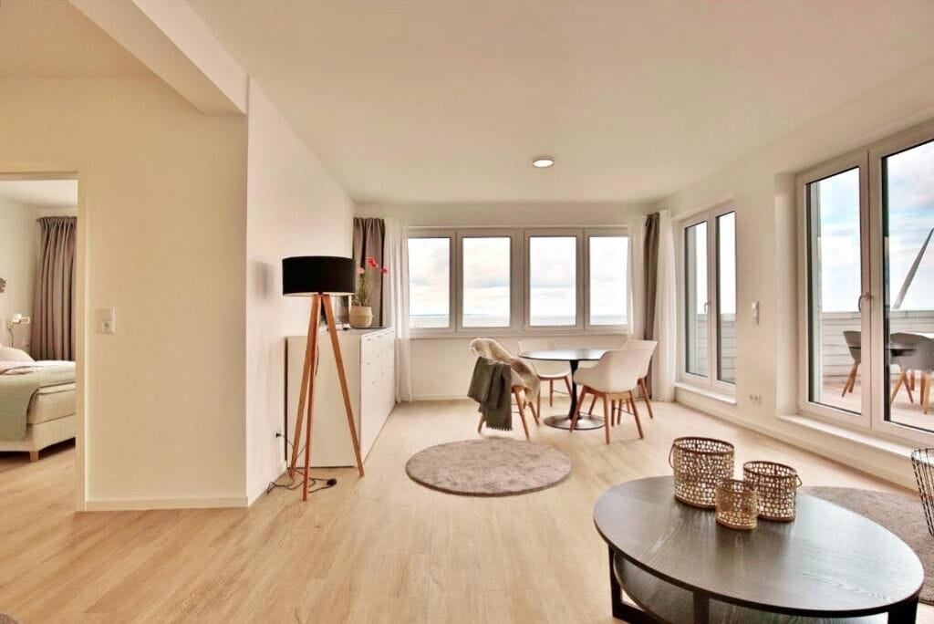 A modern living room with a dining area, large windows, and a flat-screen TV.