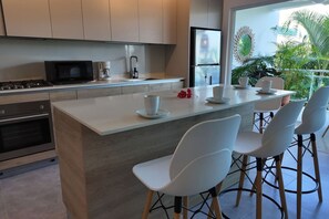 A modern kitchen with a central island, white bar stools, and a view of greenery outside. - 3 Bedroom Beachfront Apartment (Las Terrenas)