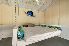 Ein Bett mit weißer Matratze und farbenfrohen Kissen, ein blauer Fisch an der Wand befestigt, und Holzpaneele an Wänden und Decke.