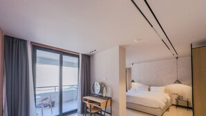 Ein modernes Hotelzimmer mit großem Balkon, Schreibtisch mit Stuhl, Bett und Nachttisch.