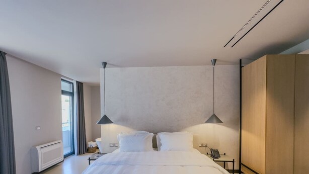 Ein modernes Hotelzimmer mit einem großen Bett, zwei Nachttischlampen, einem Telefon am Nachttisch und Blick ins Freie durch ein Fenster.