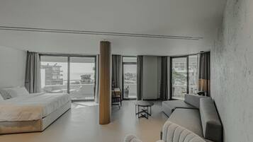Ein modernes Hotelzimmer mit einem großen Bett, einer Sitzecke mit Sofa und Sesseln, einem kleinen Tisch und Blick auf die Stadt durch große Fenster.