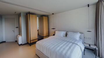 Moderni hotellihuone, jossa on suuri sänky, vaatekaappi, yöpöytä ja kaukosäädin.