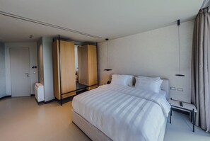 Ein modernes Hotelzimmer mit einem großen Bett, einem Schrank, einem Nachttisch und einer Fernbedienung.