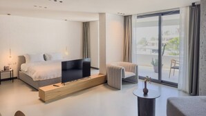 Ein modernes Hotelzimmer mit einem großen Bett, einem Flachbildfernseher, einer Sitzecke mit einem Sessel und einem kleinen Tisch sowie einem Balkon mit Blick auf die Stadt.