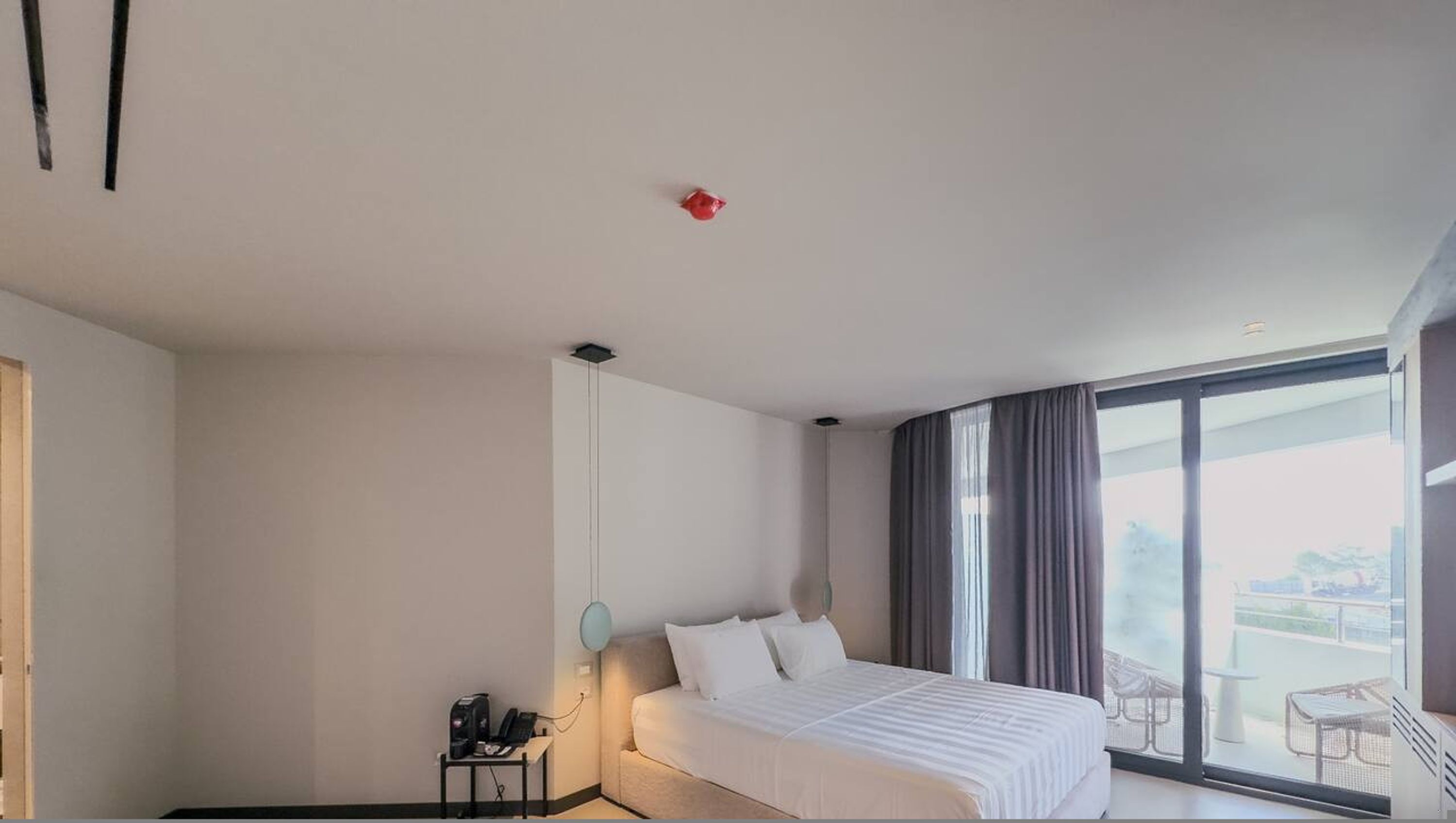 Una camera d'albergo moderna con un letto grande, una scrivania piccola con un telefono e un balcone con mobili da esterno.