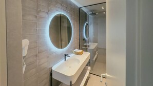 Een moderne badkamer met een grote spiegel, een witte wastafel en een douche met glazen wanden.