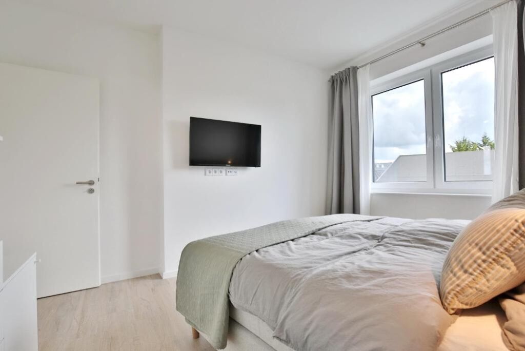 A bedroom with a bed, a TV mounted on the wall, a window with curtains, and a door.